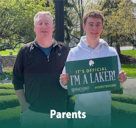 A dad posing with his son who has decided to attend 紫ý. The son holds a poster reading "It's Official. I'm a Laker!"